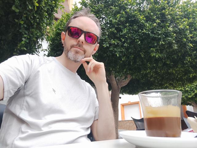 Selfie of me (middle-aged man) at a cafe after a cycle with a cortado in front of me.