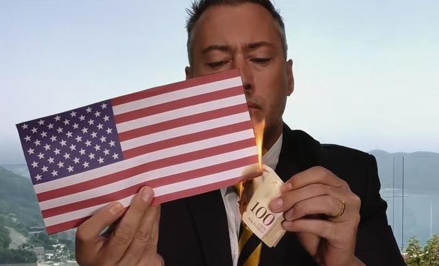 Jeff Berwick setting a printout of an American flag on fire with a 100 Bolivar note