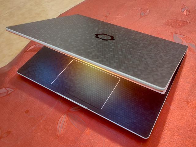 My Framework 13 on a table with its lid slightly open, casting an orange glow on the palm rest. It has an orange bezel and a black DBrand skin.